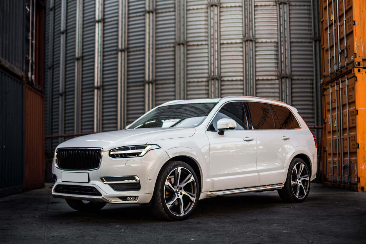 Ein weißer SUV steht zwischen großen Metallcontainern in einem Industriegebiet